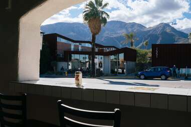 a can of beer on the bar facing out an open window towards the mountains and palm trees in palm springs, ca