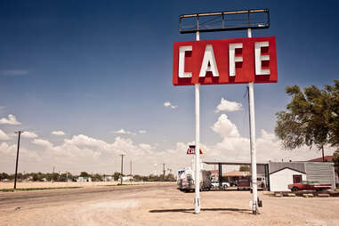 a roadside sign that says CAFE in a dusty parking lot with a vintage look