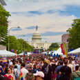 A large crowd of people celebrating Pride march in front of the Capitol building.